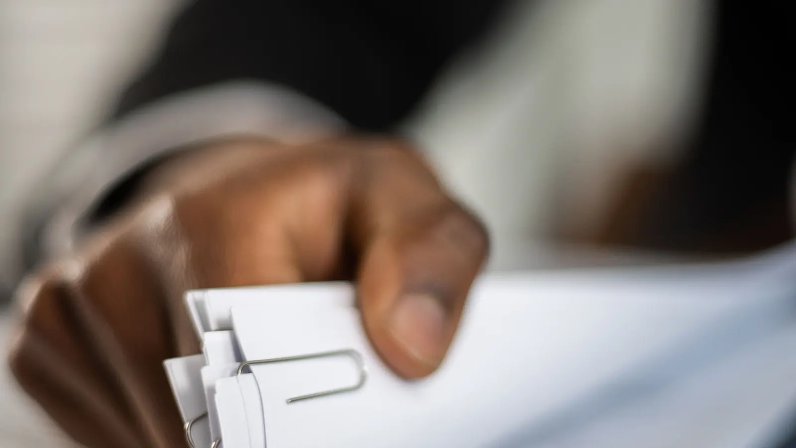 Close-up of a hand holding a stack of documents with paper clips